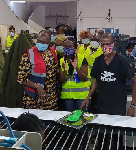 From left: Industrialization CS Betty Maina, Navalayo and a worker look at shoes in the production line at Umoja Rubber Company in October,2020.