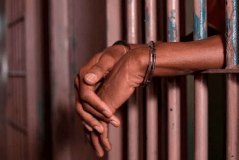 Hands resting on jail bars at a police station.