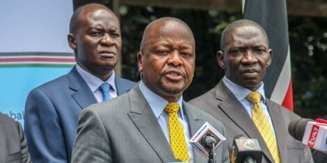 Health CS Mutahi Kagwe (centre) addresses the press in April 2020 alongside Health Director-General Patrick Amoth (behind) and Government Spokesperson Cyrus Oguna (right)