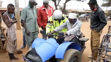 Residents look on as Philip Kivuva teaches a cobbler how to operate a motorized tricycle he designed