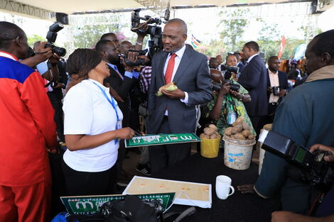 Trade Cabinet Secretary Moses Kuria (centre) enjoys roasted maize while interacting with traders at the Green Park Terminus ahead of the official launch of the Hustlers' Fund on November 30, 2022. 