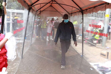 Nairobi residents use a sanitiser spray booth installed by the Sonko Rescue Team at the Kencom bus stage, April 19, 2020.