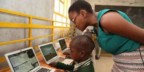 Nelly Cheboi teaching a young boy to use a computer.