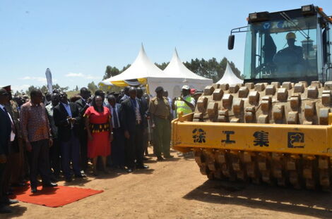 President Uhuru Kenyatta look on as a road compactor compresses a road in Nakuru County.