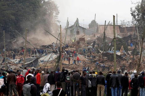 Residents looking helplessly as a bulldozer pulls down their houses.